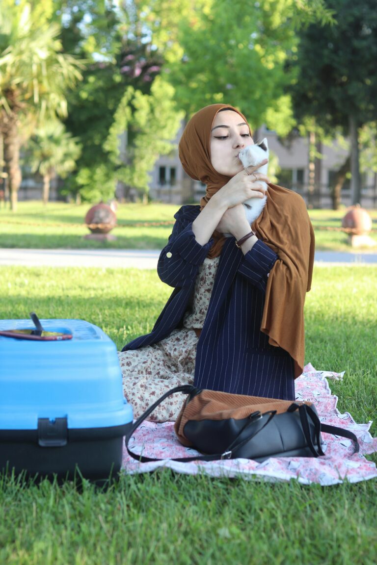 A woman sitting on green grass, enjoying a sunny day outdoors, with a best cat carrier & relaxed expression on her face.