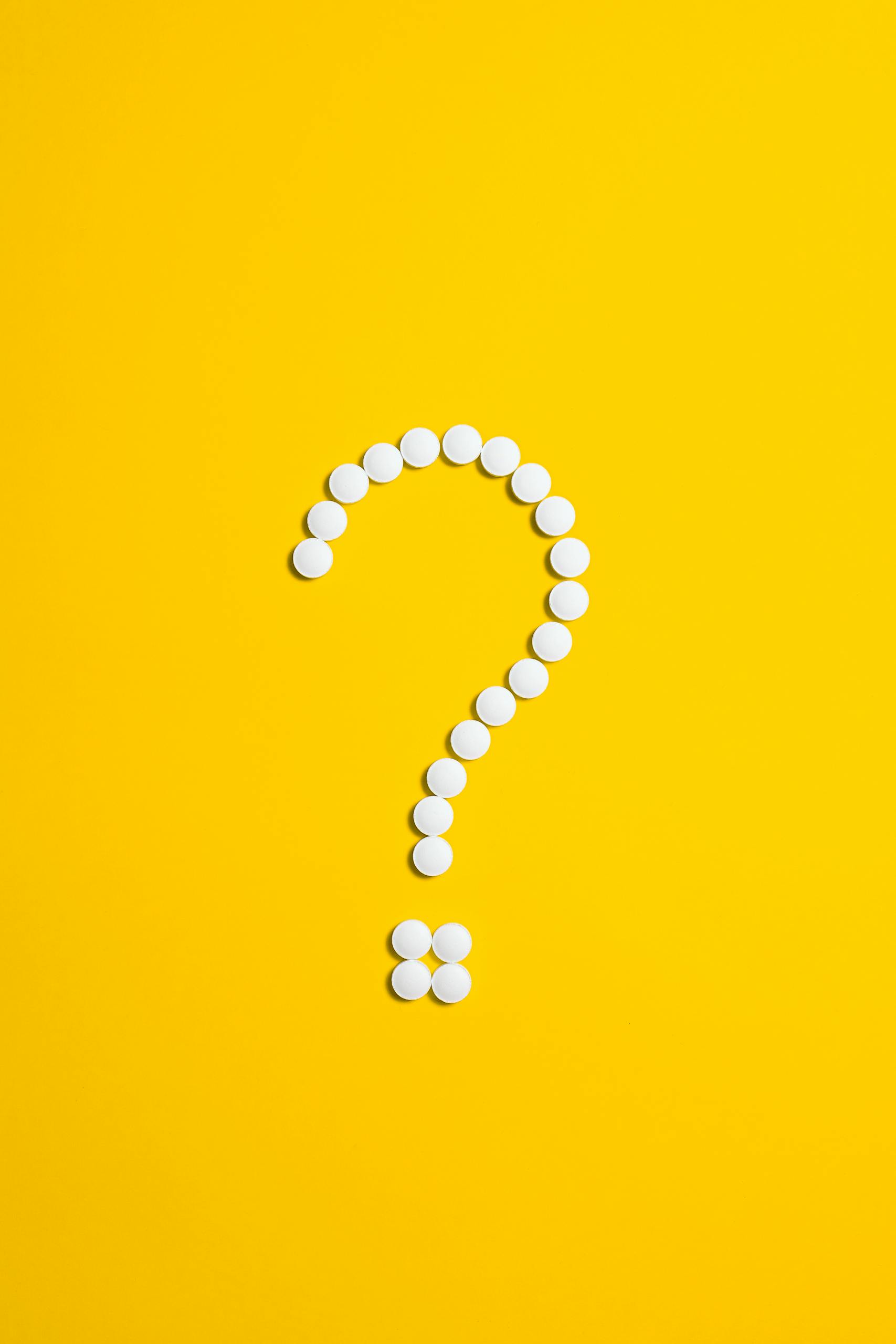 Home Page 8 White pills arranged in a question mark shape on a bright yellow background, symbolizing medical queries.